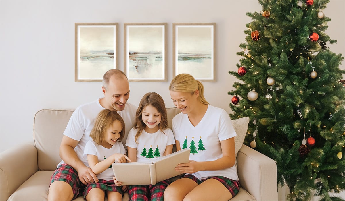 Happy family sitting on a couch, looking at a photo album, all wearing matching Christmas pyjamas, in a living room decorated for Christmas and wall art poster frames on the wall.